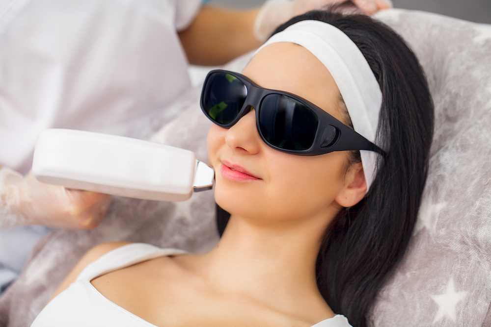 A female patient with protective glasses smiles during laser skin resurfacing in Sterling Heights