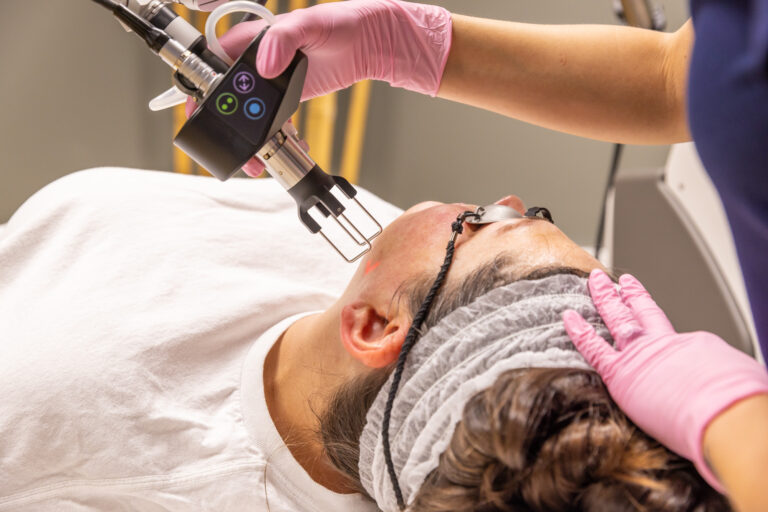 A woman lying on a treatment bed while a gloved medical provider administers one of Tri-County's best Facials near Macomb, MI.